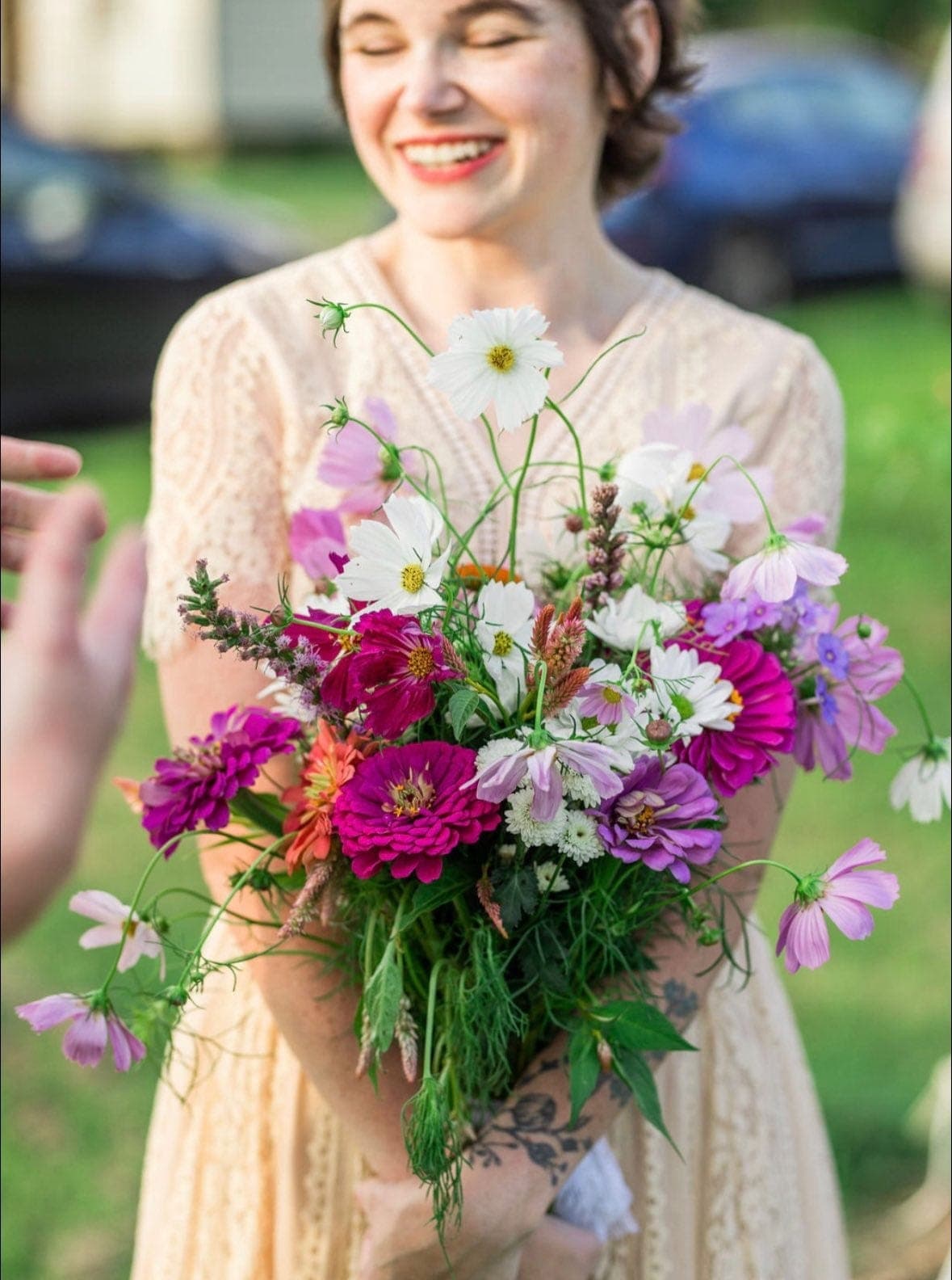 Bride in lace dress holding loose wildflower bridal bouquet with cosmos, zinnias, and celosia